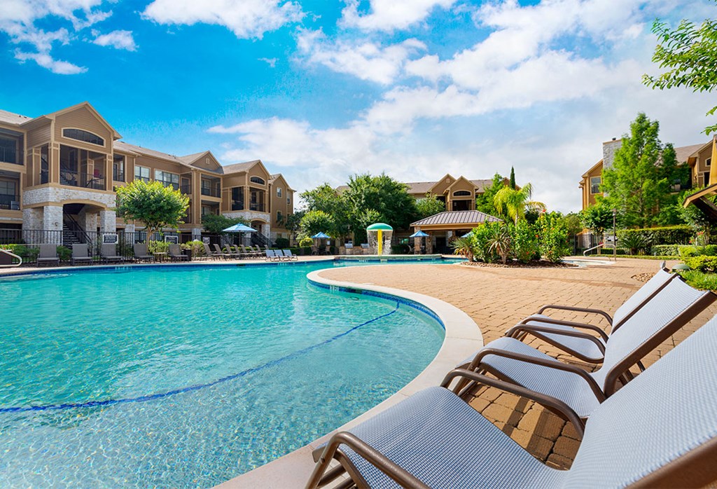a swimming pool with lounge chairs in front of an apartment building