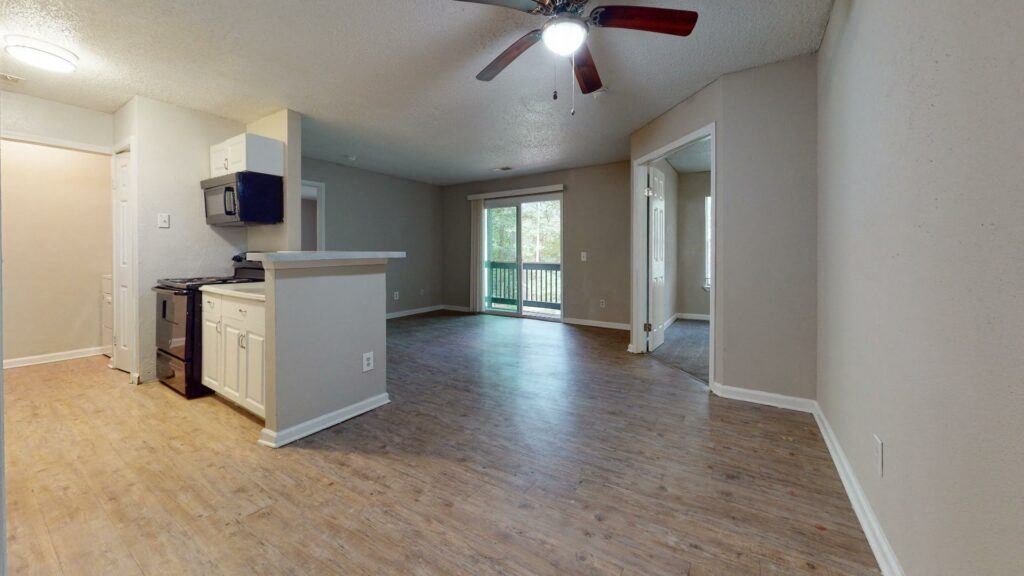an empty living room with a kitchen and a ceiling fan