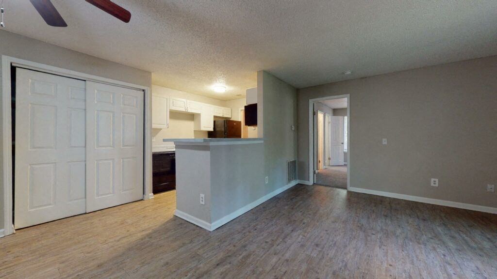 an empty living room with a kitchen in the background