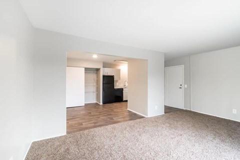 an empty living room with a kitchen in the background