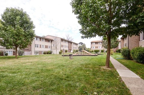 a park with grass and trees in front of apartment buildings