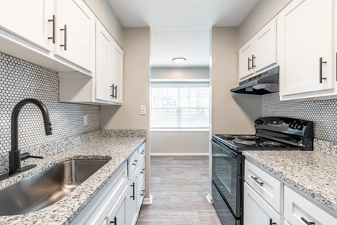 A kitchen with white cabinets and a black and white tiled backsplash.