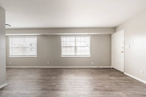 A spacious room with wooden floors and two windows.