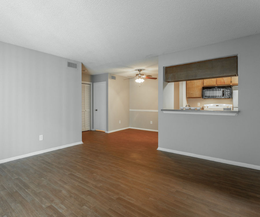 an empty living room with a kitchen and a ceiling fan