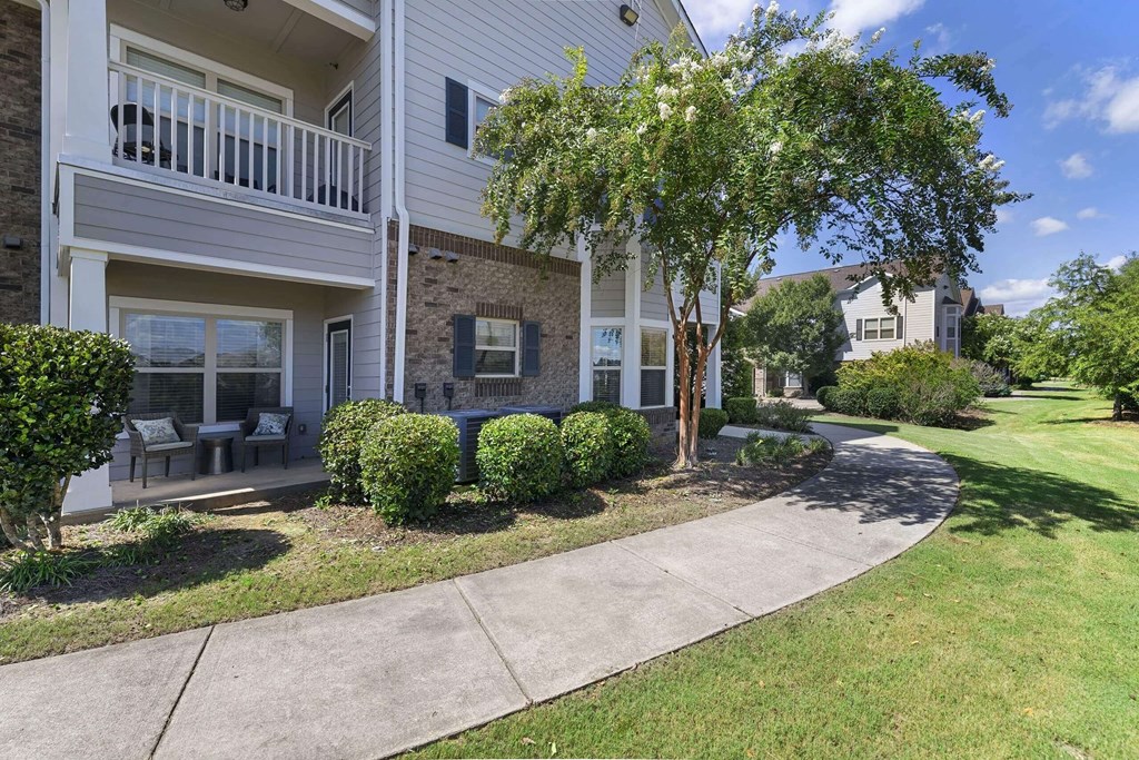 a sidewalk in front of a building with trees and bushes