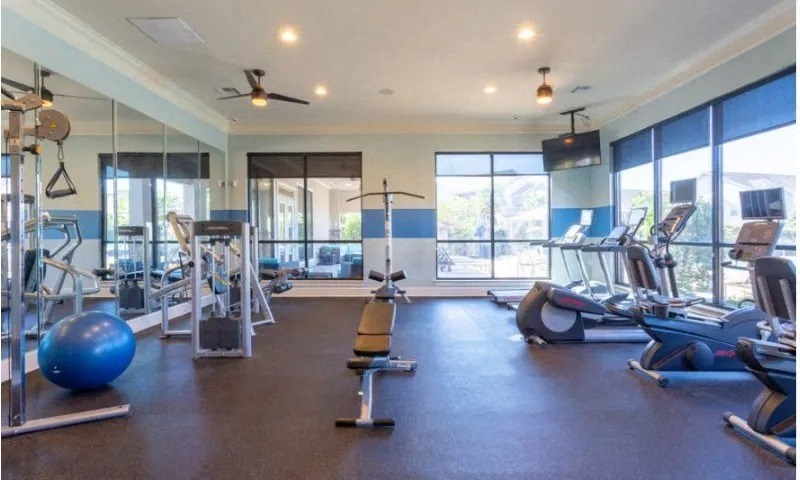 a gym with cardio machines and weights on the floor and large windows at Century HomePlace, Prattville, AL
