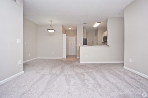 the living room and kitchen of an empty home with carpeted flooring