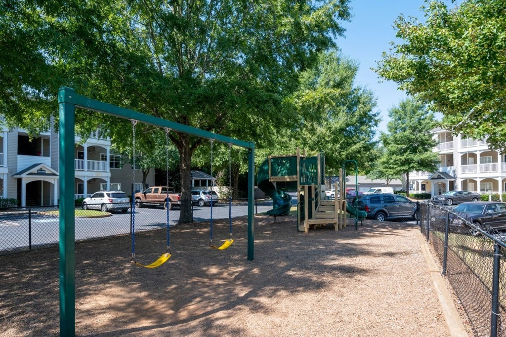 A playground with a swing set and a slide in the middle of a parking lot.