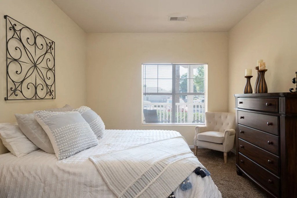 A bedroom with a large bed, a chair, and a dresser.