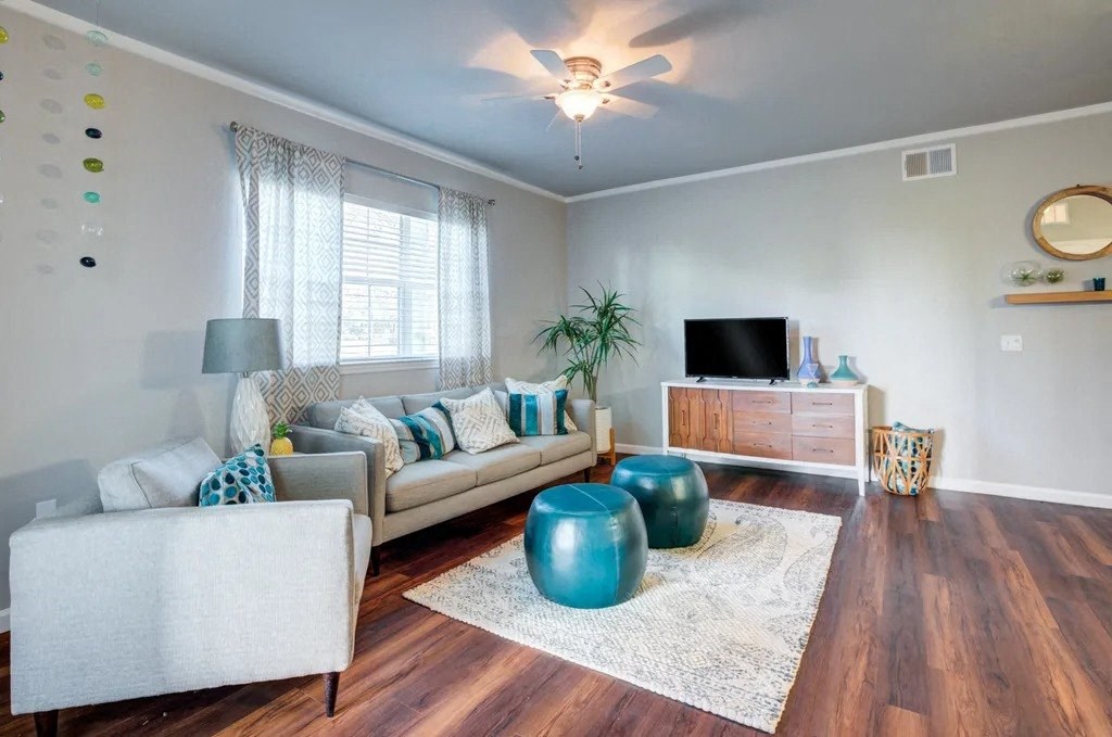 A living room with a white couch, a blue ottoman, and a wooden floor.at Century Ariva, Lakeland, 33812  