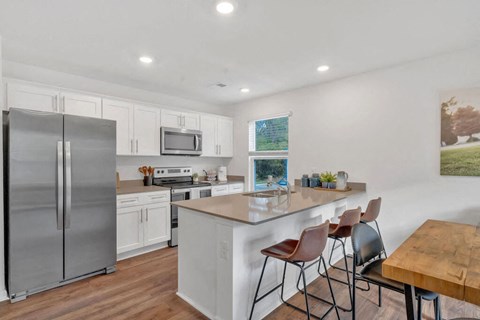 A kitchen with a refrigerator, microwave, oven, and sink.
