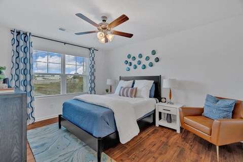 A bedroom with a bed, chair, and ceiling fan.