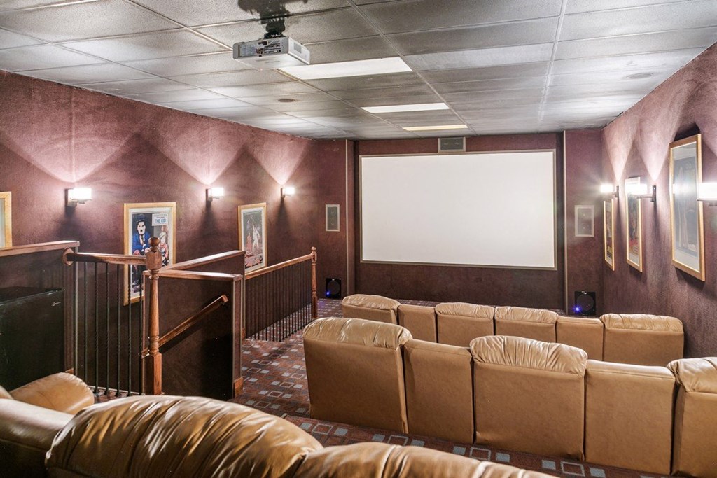 A row of brown leather seats are arranged in front of a large screen in a theater room at Ridge Crossings Apartments, Hoover, AL 35244