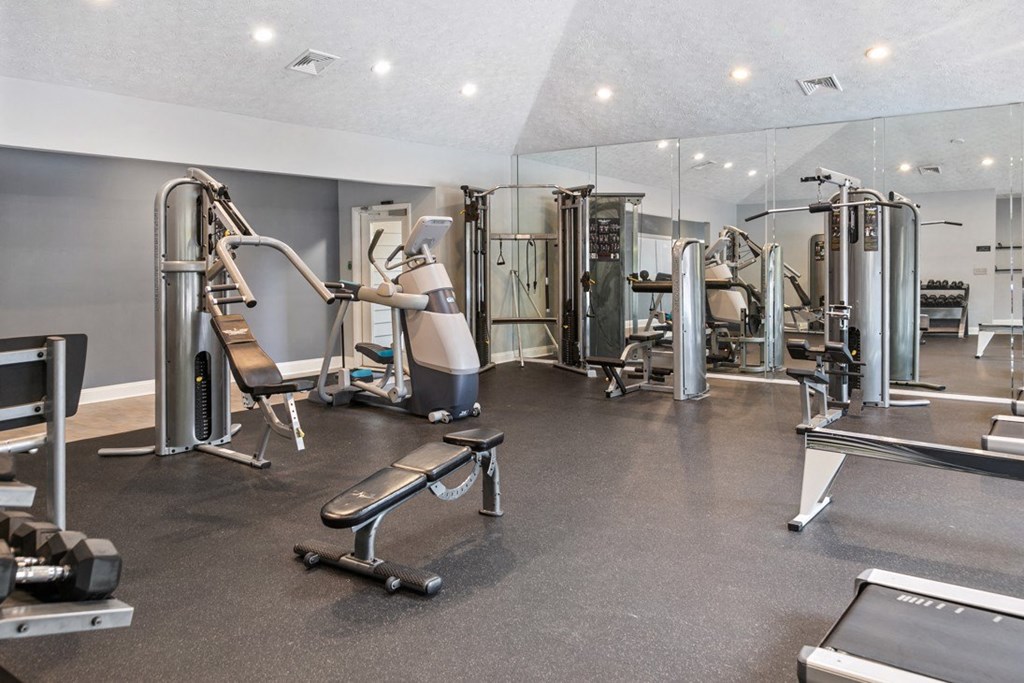 A spacious gym with a variety of equipment including a treadmill, weight bench, and leg press machine at Ridge Crossings Apartments, Alabama
