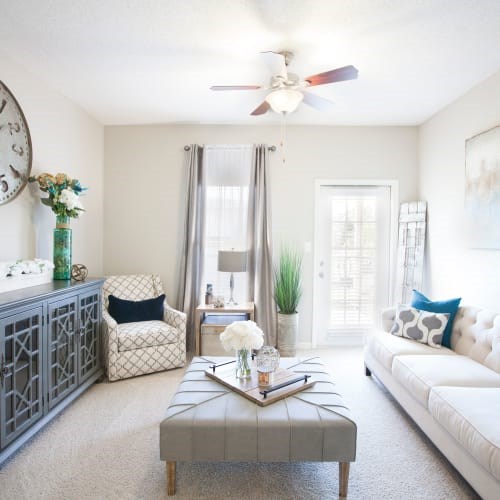 A living room with a grey ottoman and a white sofa.