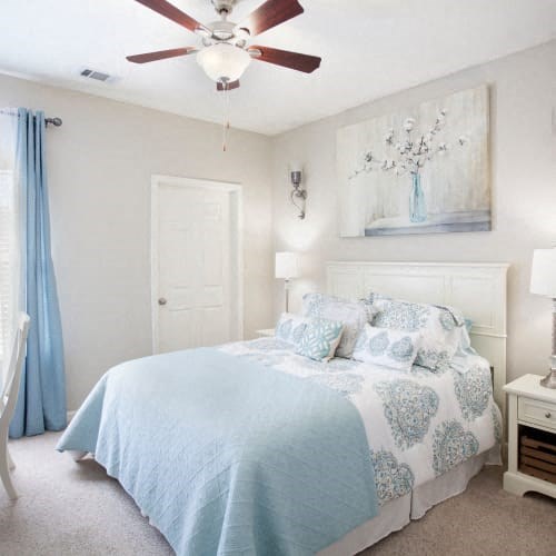 A bedroom with a bed, a ceiling fan, and a painting on the wall.