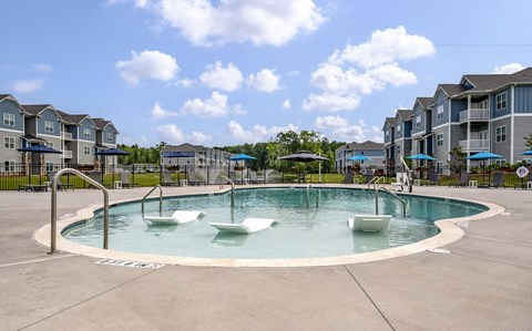 A round swimming pool with four white loungers in the middle of it.