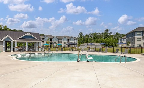 A large swimming pool surrounded by a concrete patio and a fence with a residential area in the background.