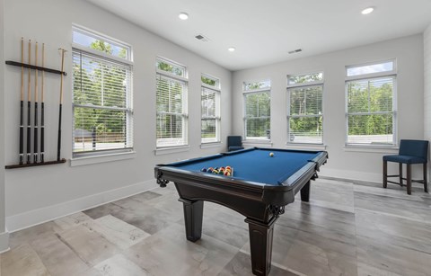 A pool table is in the middle of a room with a chair and windows.