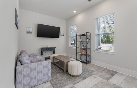 A living room with a grey couch, a coffee table, a television, and a window with blinds.