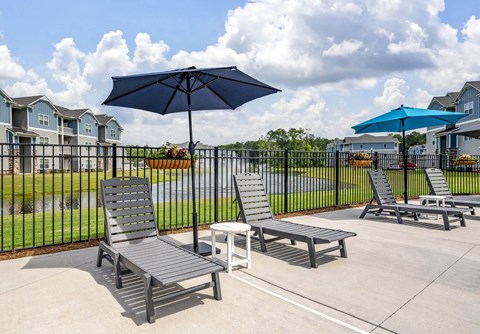 A patio with a black umbrella, two chairs and a bench.