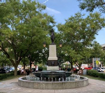A statue of a man holding a torch stands atop a fountain in a park.