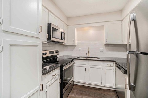 A kitchen with white cabinets and black countertops.