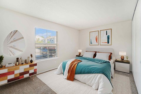 A bedroom with a bed, nightstand, and a window with blinds.