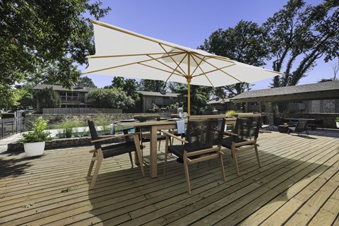 A wooden table with chairs and a large umbrella on a wooden deck.