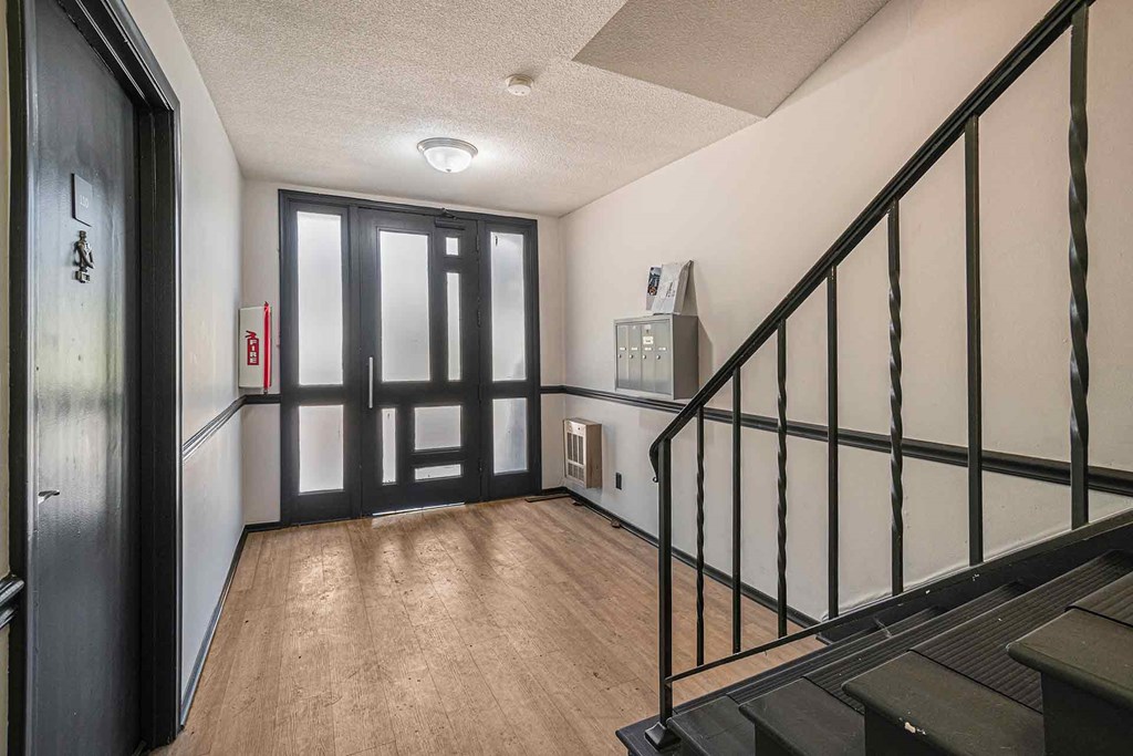 A hallway with a black railing and wooden flooring.