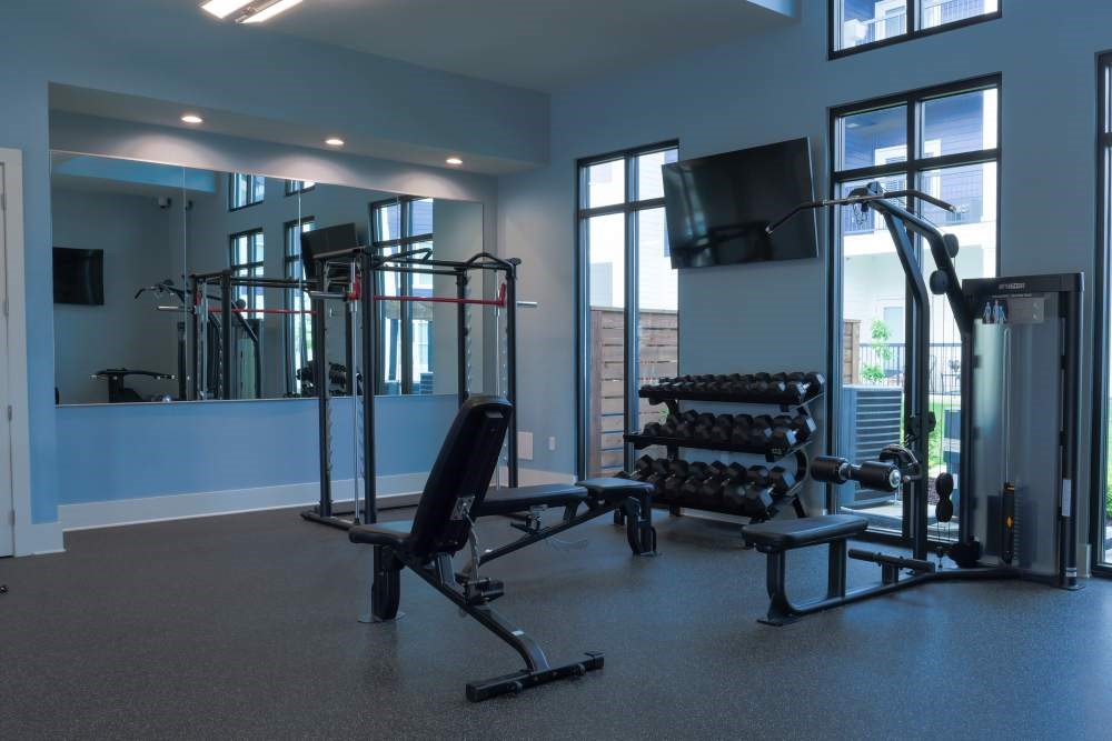 A gym with a variety of equipment including a bench, weights, and a television.