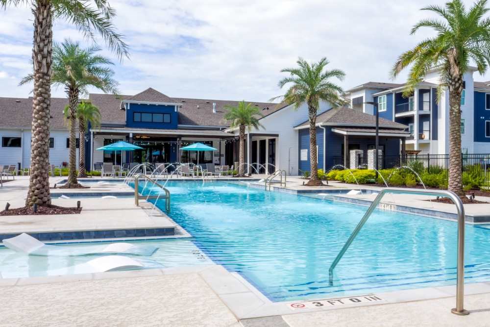 A pool surrounded by palm trees and a building in the background.
