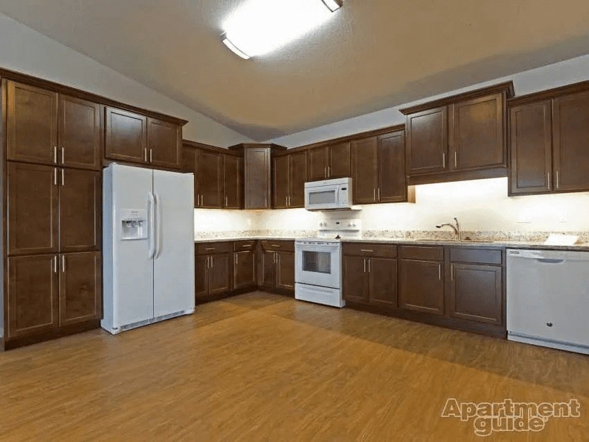 Apartment Guide logo on a kitchen with brown cabinets and white appliances.