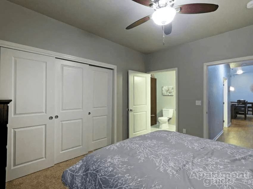 A bedroom with a bed, a ceiling fan, and a door leading to a bathroom.