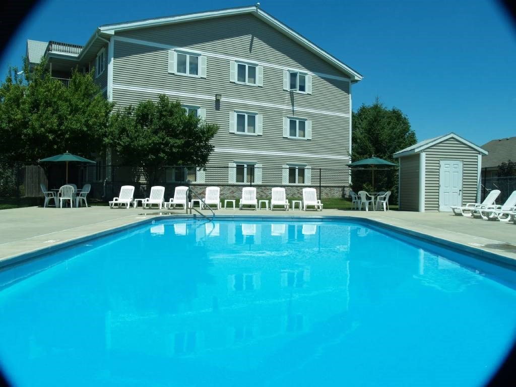 A pool in front of a grey building with white chairs around it.