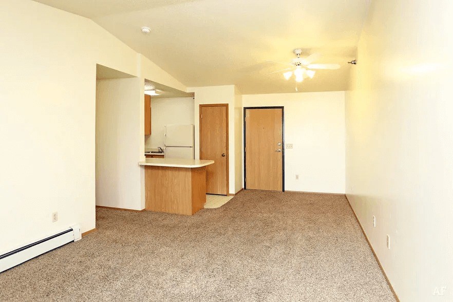 A spacious living room with a kitchenette and two doors.