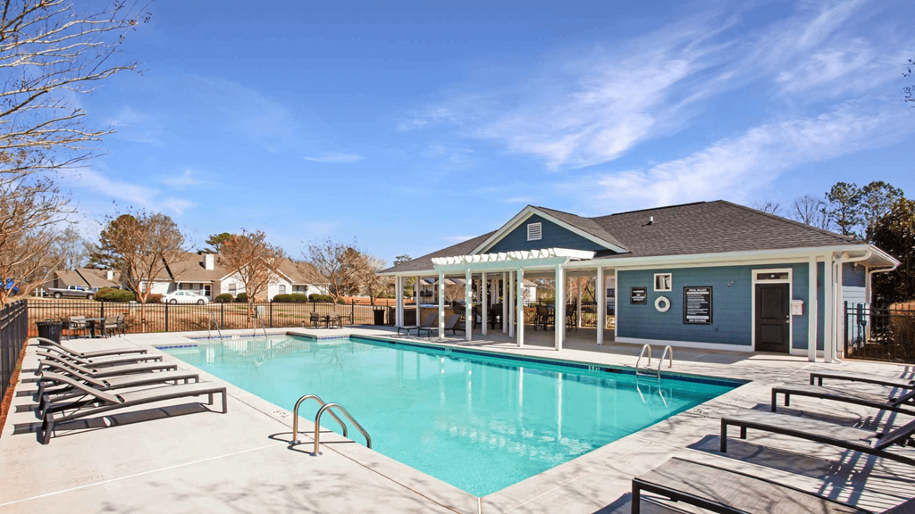 A swimming pool with sun loungers and a building in the background.