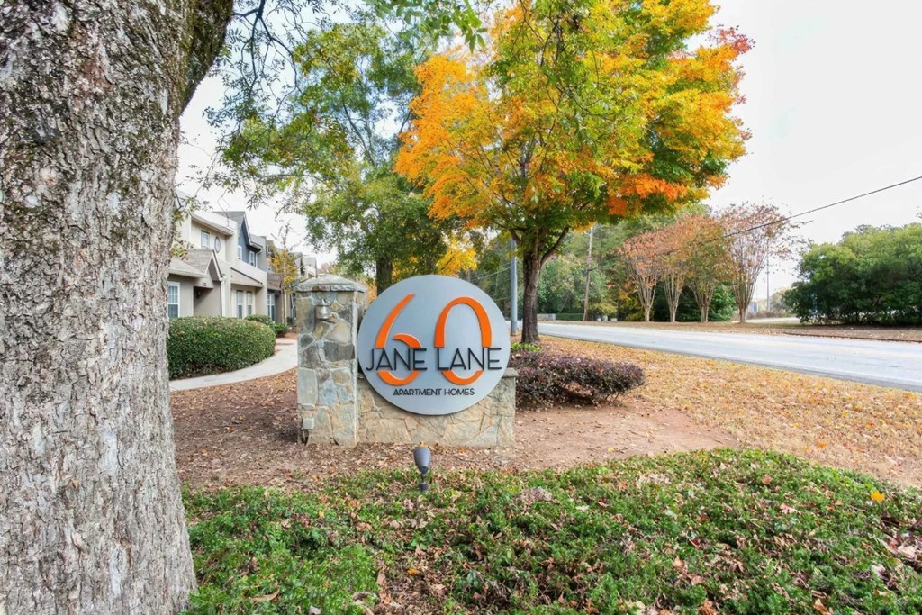 A sign for Jane Lane Apartments is in front of a tree with fall foliage.