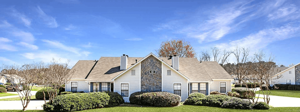 A large house with a grey roof and white walls is surrounded by a well-manicured lawn.