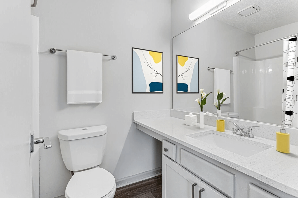 A white toilet is in a bathroom with a white sink and a white counter.