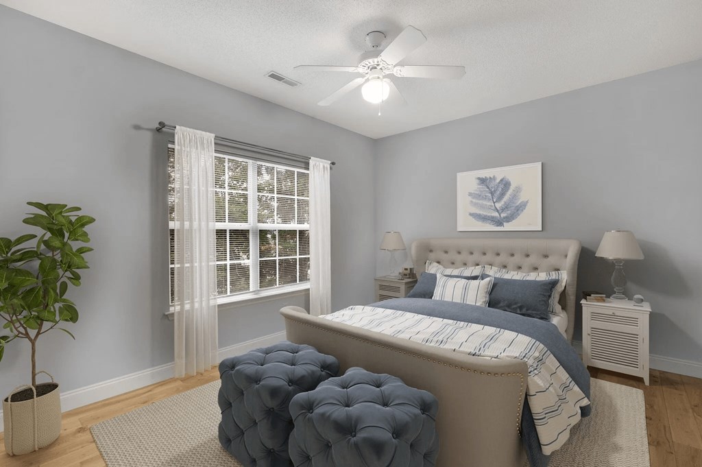 A bedroom with a large bed, a ceiling fan, and a potted plant.