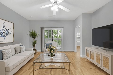 A living room with a white couch, a glass coffee table, and a television.