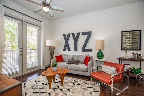A living room with a grey couch, a red chair, a wooden table, and a rug with a black and white pattern.
