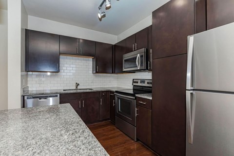 A kitchen with dark brown cabinets and a granite countertop.at Century Cedar Hill, Cedar Hill