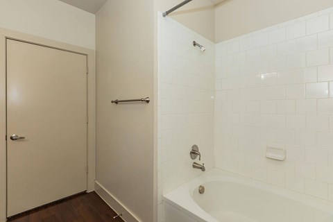 A white tiled bathroom with a bathtub and a door.at Century Cedar Hill, Texas