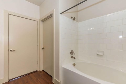 A white tiled bathroom with a bathtub and a door.at Century Cedar Hill, Texas