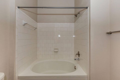 A white tiled bathroom with a white bathtub and a white toilet.at Century Cedar Hill, Cedar Hill, TX 75104