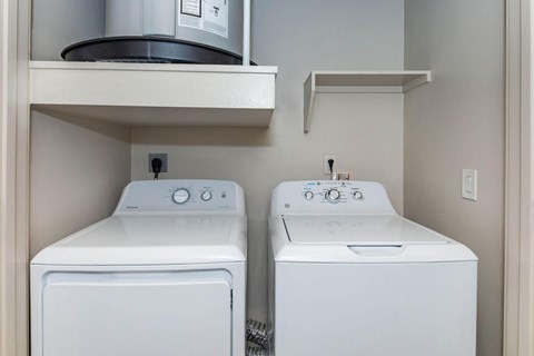 Two white front loading washing machines in a small laundry room.at Century Cedar Hill, Cedar Hill, 75104