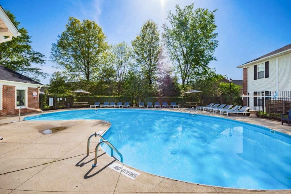 A swimming pool surrounded by trees and chairs.