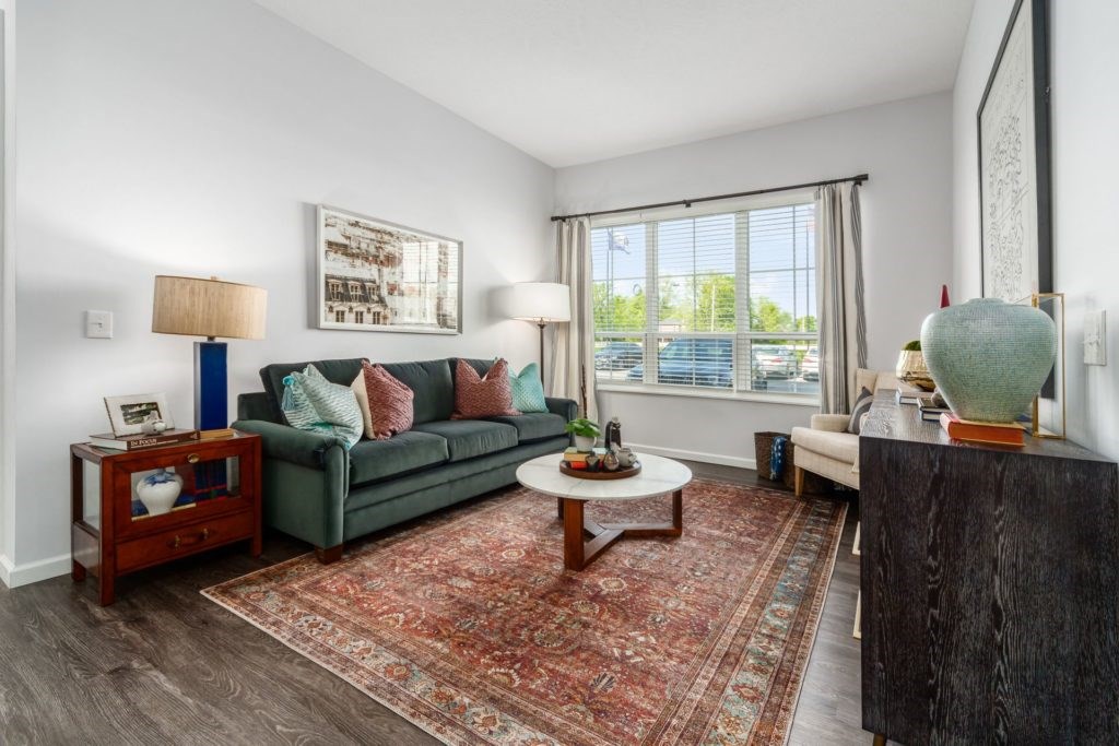 A living room with a green couch, a coffee table, and a large window.